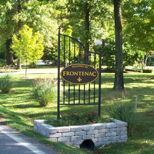 The ornamental Welcome to Frontenac sign on its stone base, set among trees at the city limits