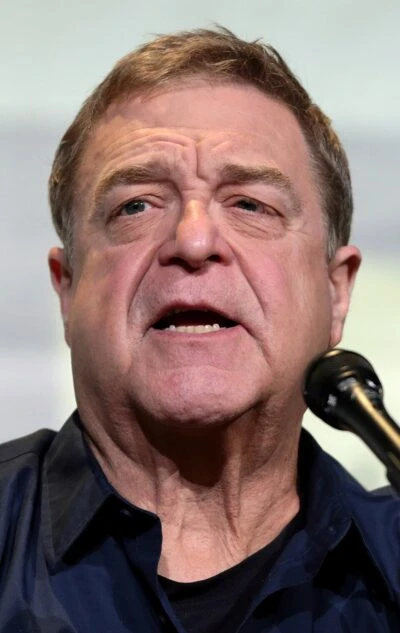 John Goodman speaking at a microphone