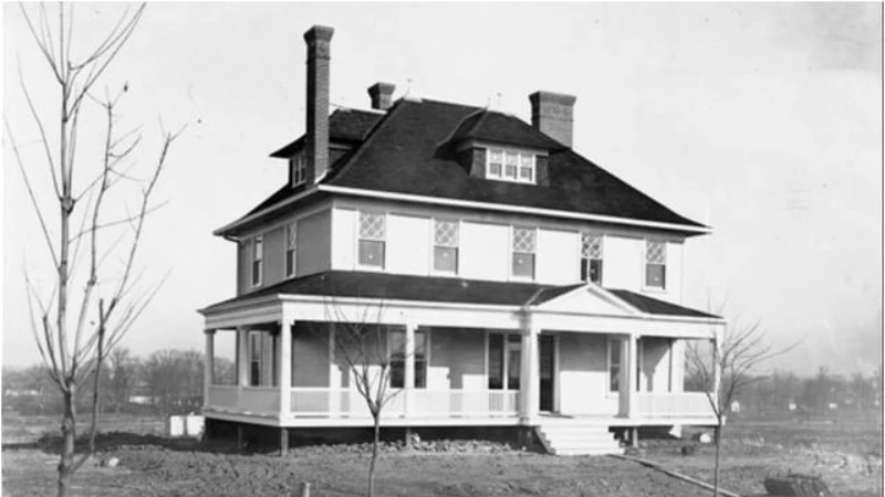 A black-and-white photograph of a two-storey house with a wraparound porch and hipped roof, one of the first built in University Heights