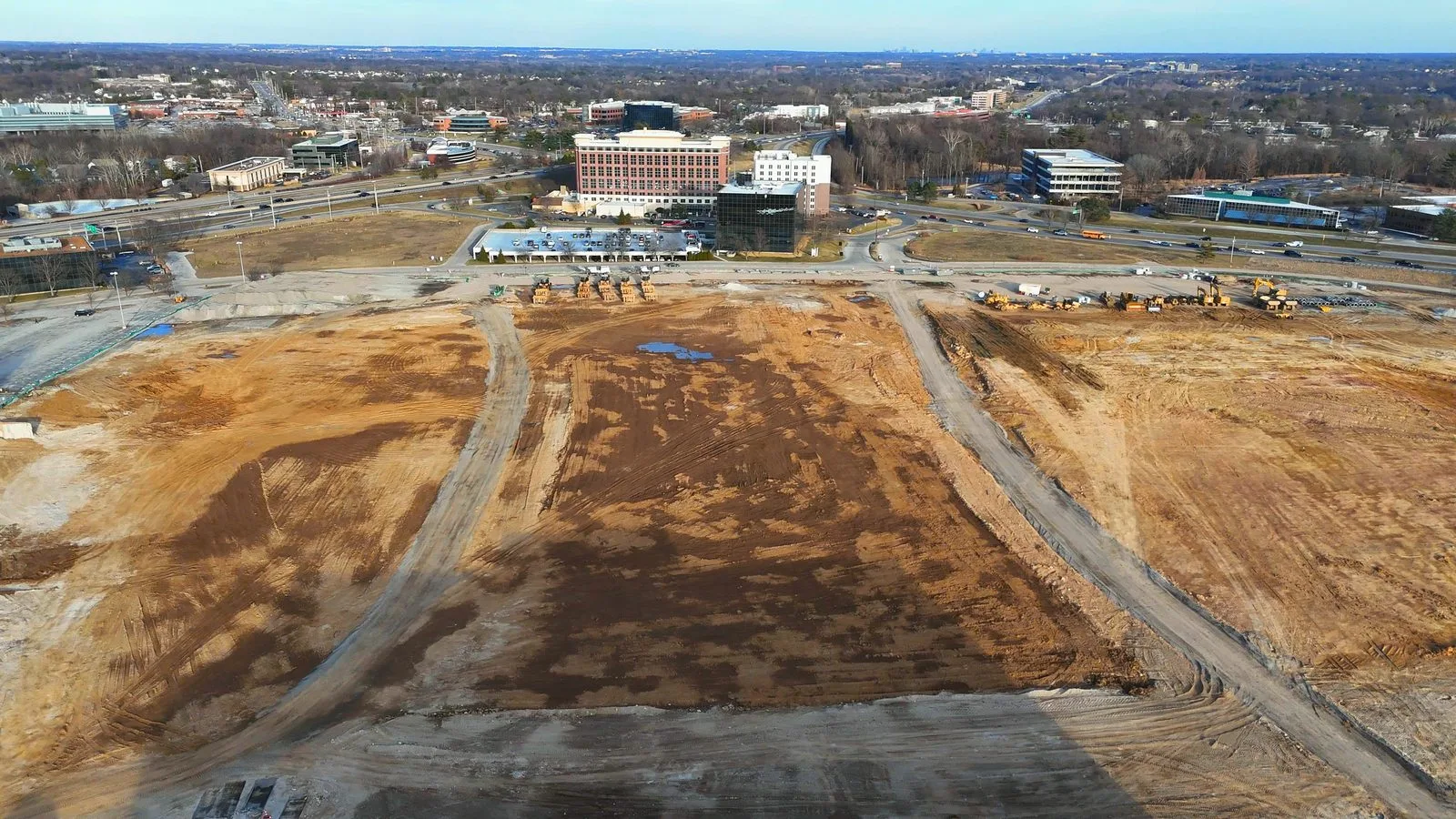 Aerial view of the graded Downtown Chesterfield site in February 2026, with the outline of the future central park cut into the dirt and the office buildings on Chesterfield Parkway behind it