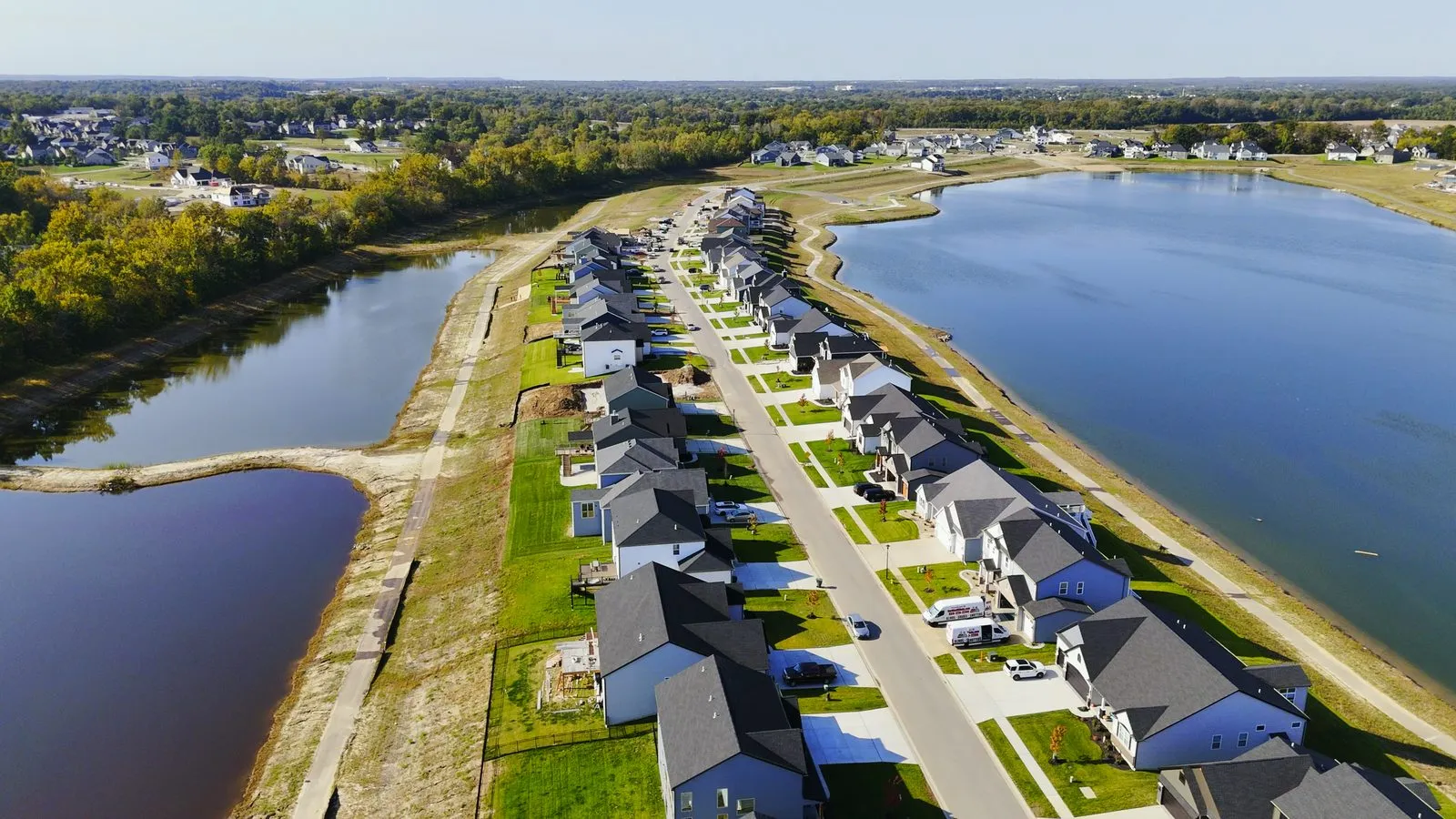 Aerial photograph looking down a Cottleville Trails street in October 2024, with a long row of completed homes on one side and one of the community lakes running alongside