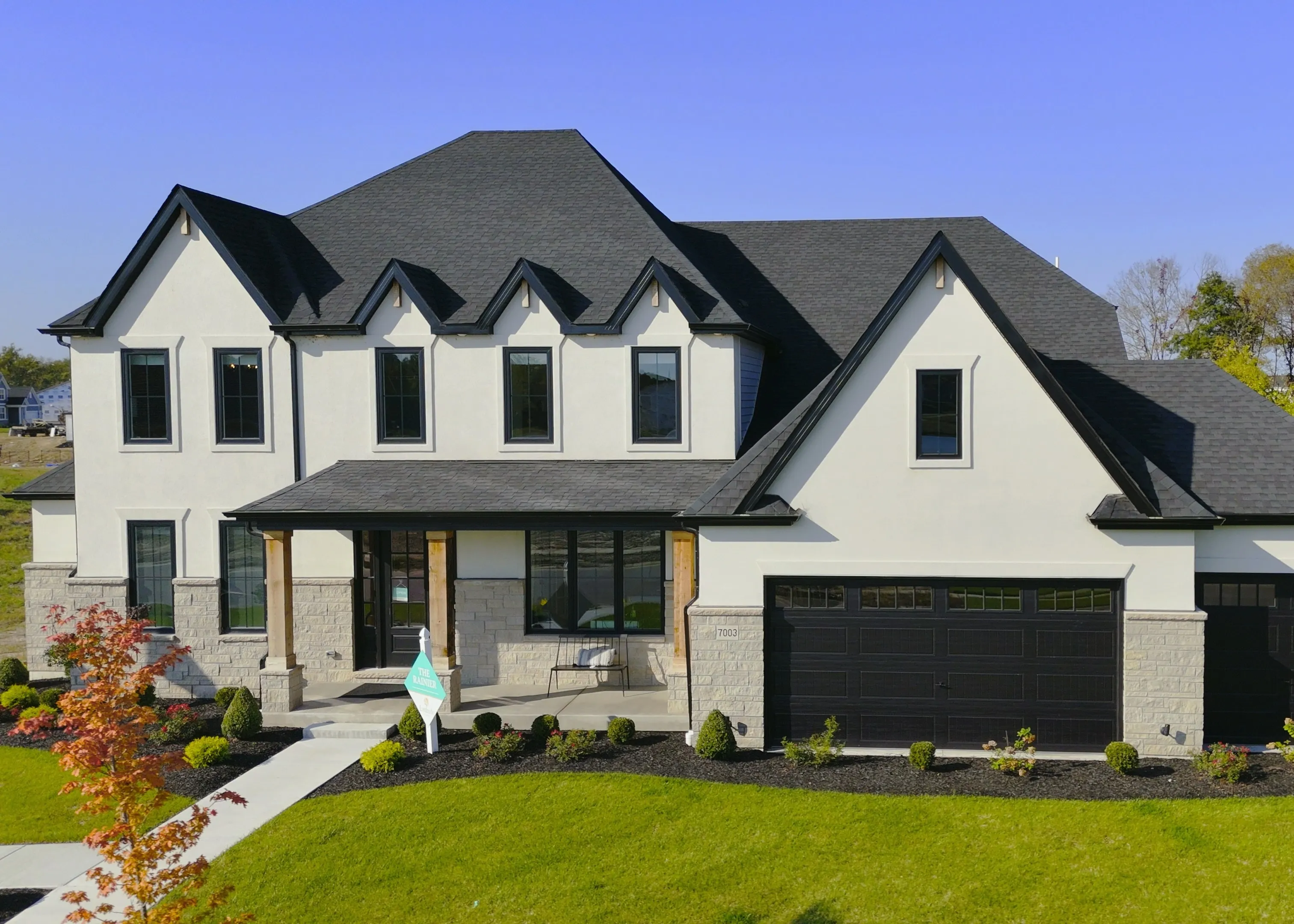A finished display home at Cottleville Trails in October 2024, two storeys in white stucco and stone with a three car garage, photographed from the street on an autumn afternoon