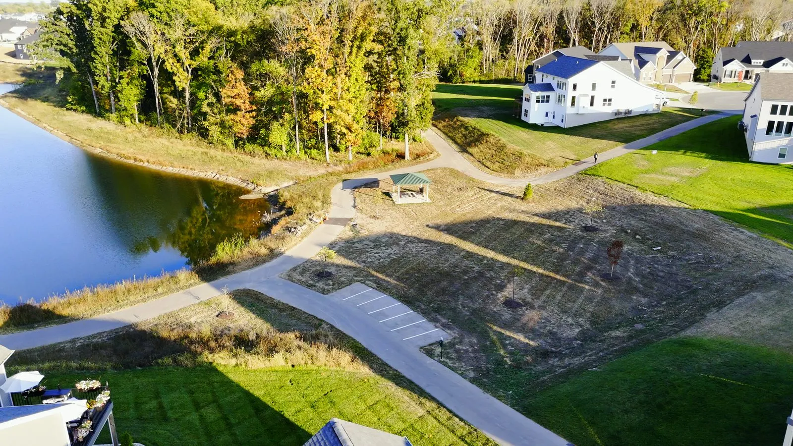 A paved walking trail beside one of the Cottleville Trails lakes in October 2025, with a small golf cart parking area alongside it
