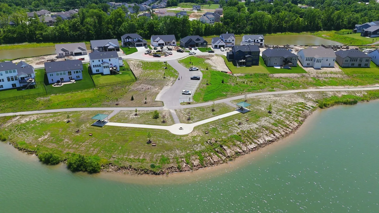 Aerial photograph of paved walking trails and a lakeside pavilion at Cottleville Trails in May 2026, with homes along the far shore