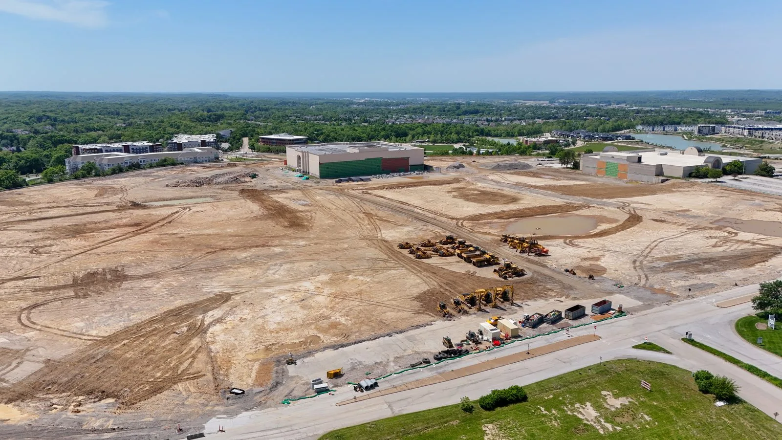 Aerial view of the graded Downtown Chesterfield site in May 2026, with earthmoving equipment on the former Chesterfield Mall footprint and the retained Dillard's and Macy's buildings in the background