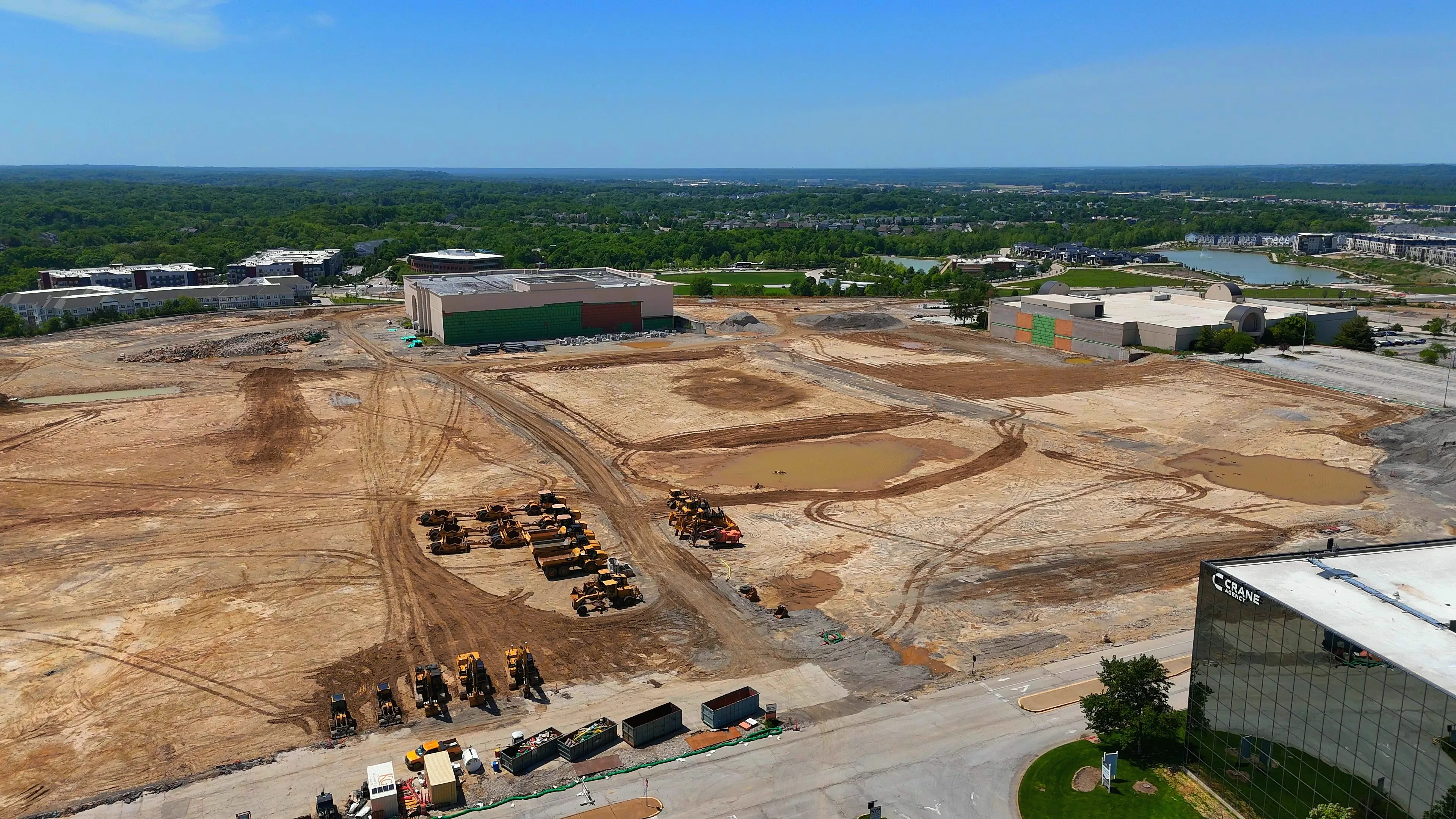 Aerial photo of the same site in May 2026, graded to bare earth with the outline of the future central park shaped into the ground