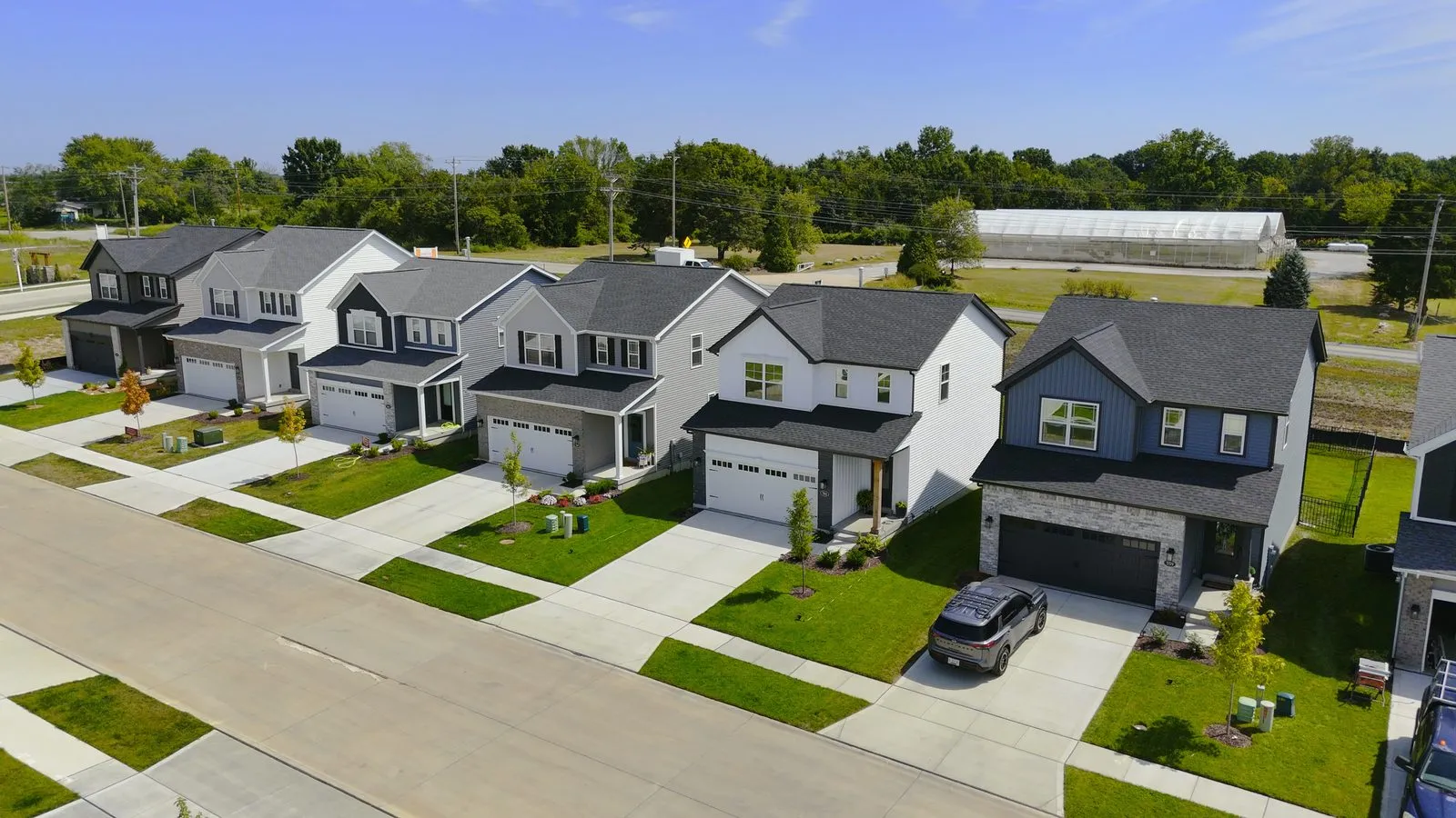 A row of completed cottage homes built by Fischer & Frichtel at Harvest in August 2025, compact two-story houses with two-car garages along a new street