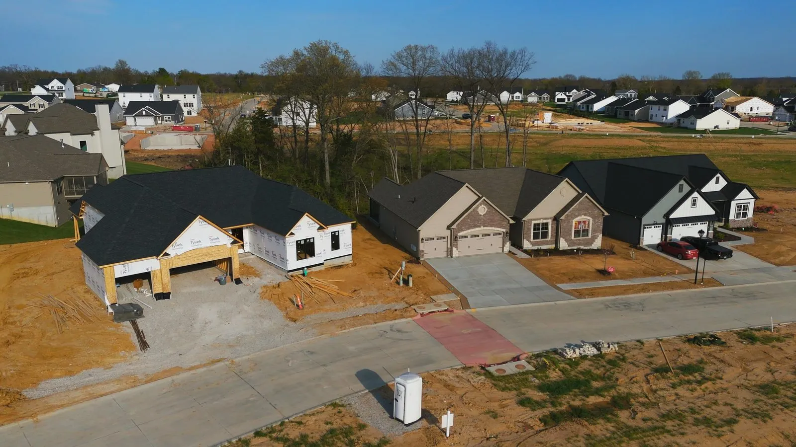 Aerial photograph of Fischer & Frichtel homes at Harvest in April 2026, finished houses beside one still in framing on a street that did not exist two years earlier