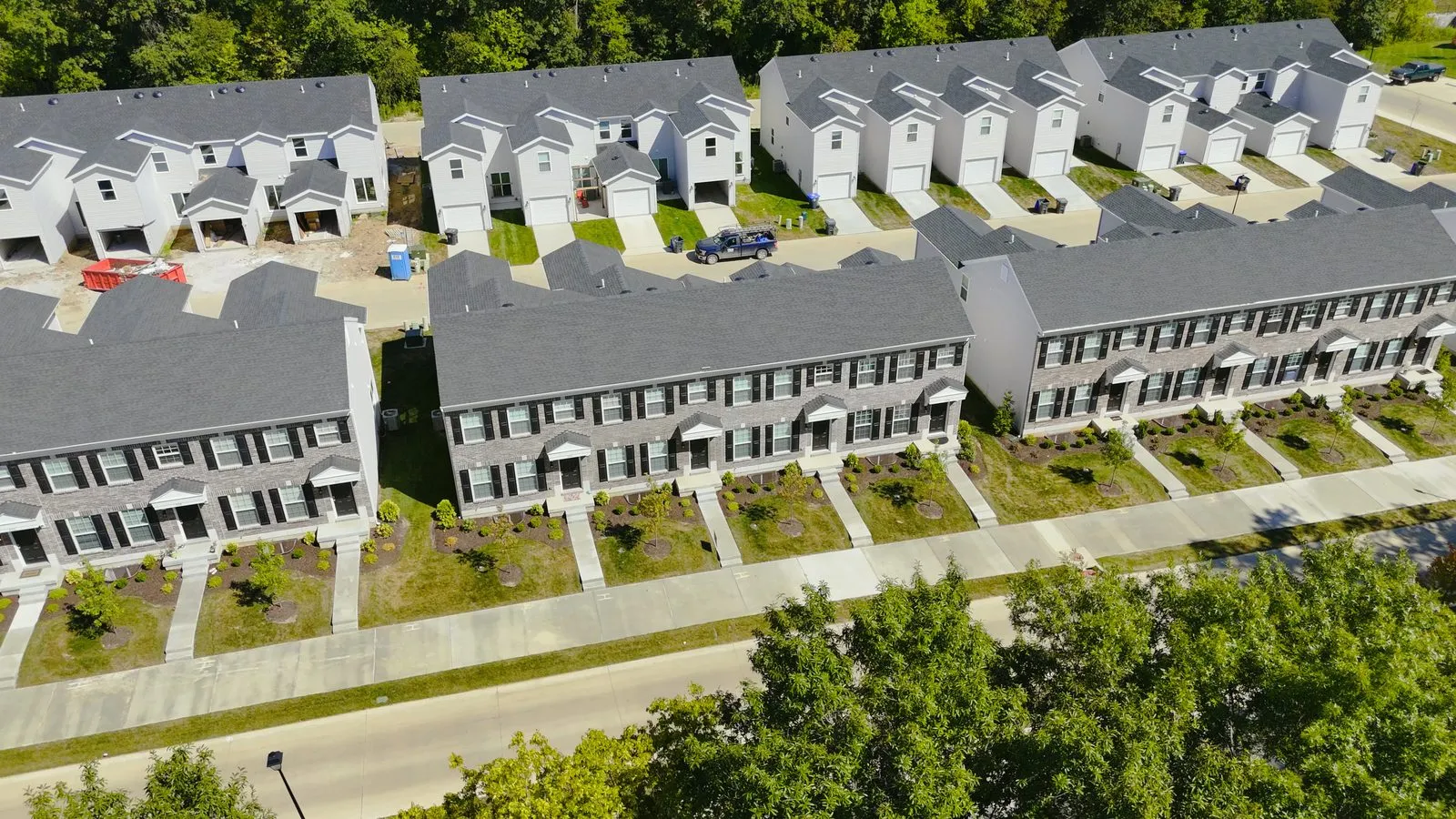 A row of completed two-story townhomes built by McBride at Harvest in August 2025, in grey and white siding with front doors facing a new street