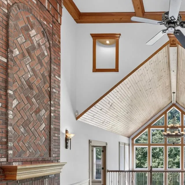 Two-story great room with a herringbone brick fireplace, vaulted wood ceiling and a wall of windows