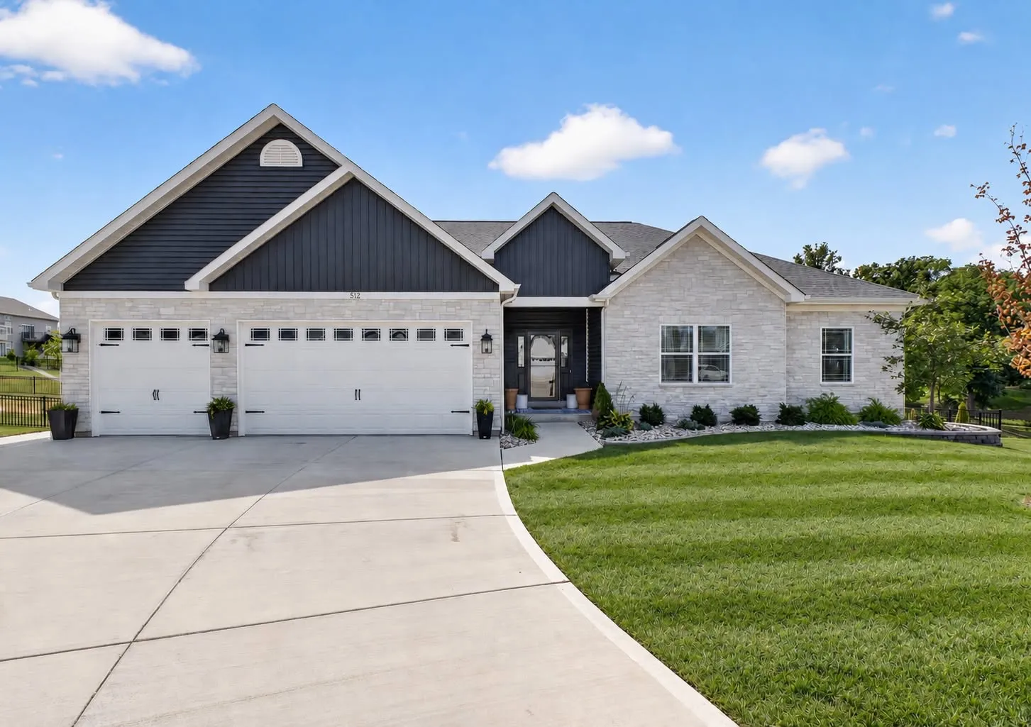 Navy board-and-batten ranch with a stone base and a three-car garage under a blue sky