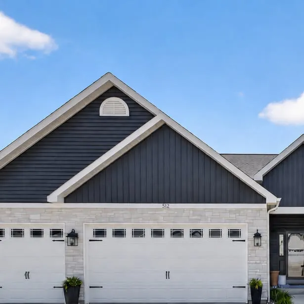 Navy board-and-batten ranch with a stone base and a three-car garage under a blue sky