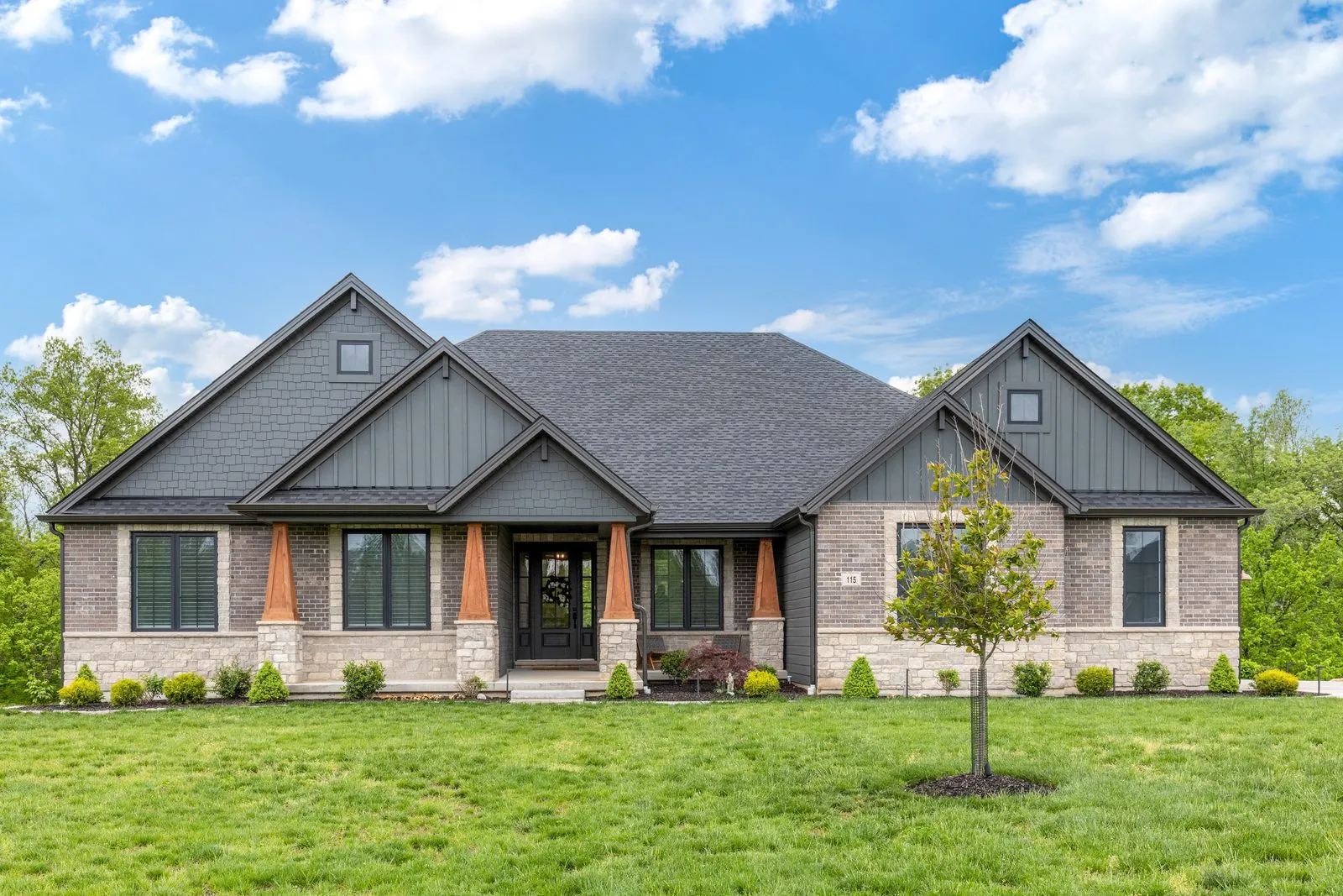 Modern craftsman new construction home exterior with dark siding and stone