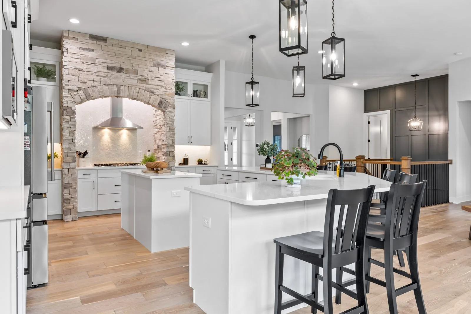 Bright white kitchen inside the same home, with a large island, stone hood and pendant lighting