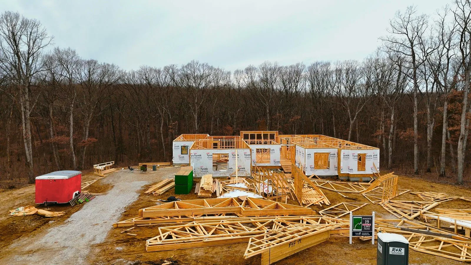 A custom home under construction at the framing stage, with roof trusses stacked in the yard