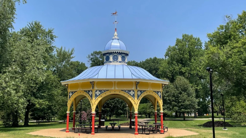 An ornate open-air pavilion in Tower Grove Park, painted yellow and blue with a domed roof and a weather vane