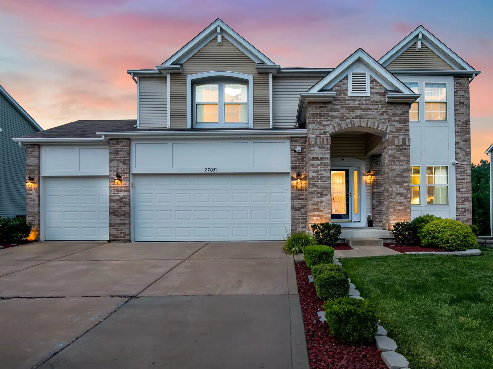Twilight photo of a two story home's front elevation with every window lit and a pink sunset sky