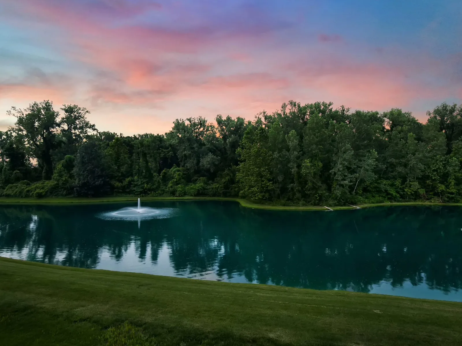 The pond and fountain behind the same home at dusk, under the same sunset sky