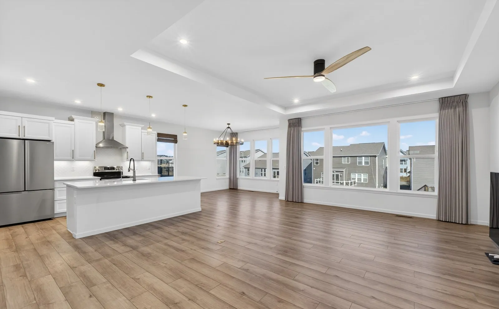 The same open plan great room and kitchen empty, with a tray ceiling and a wall of windows