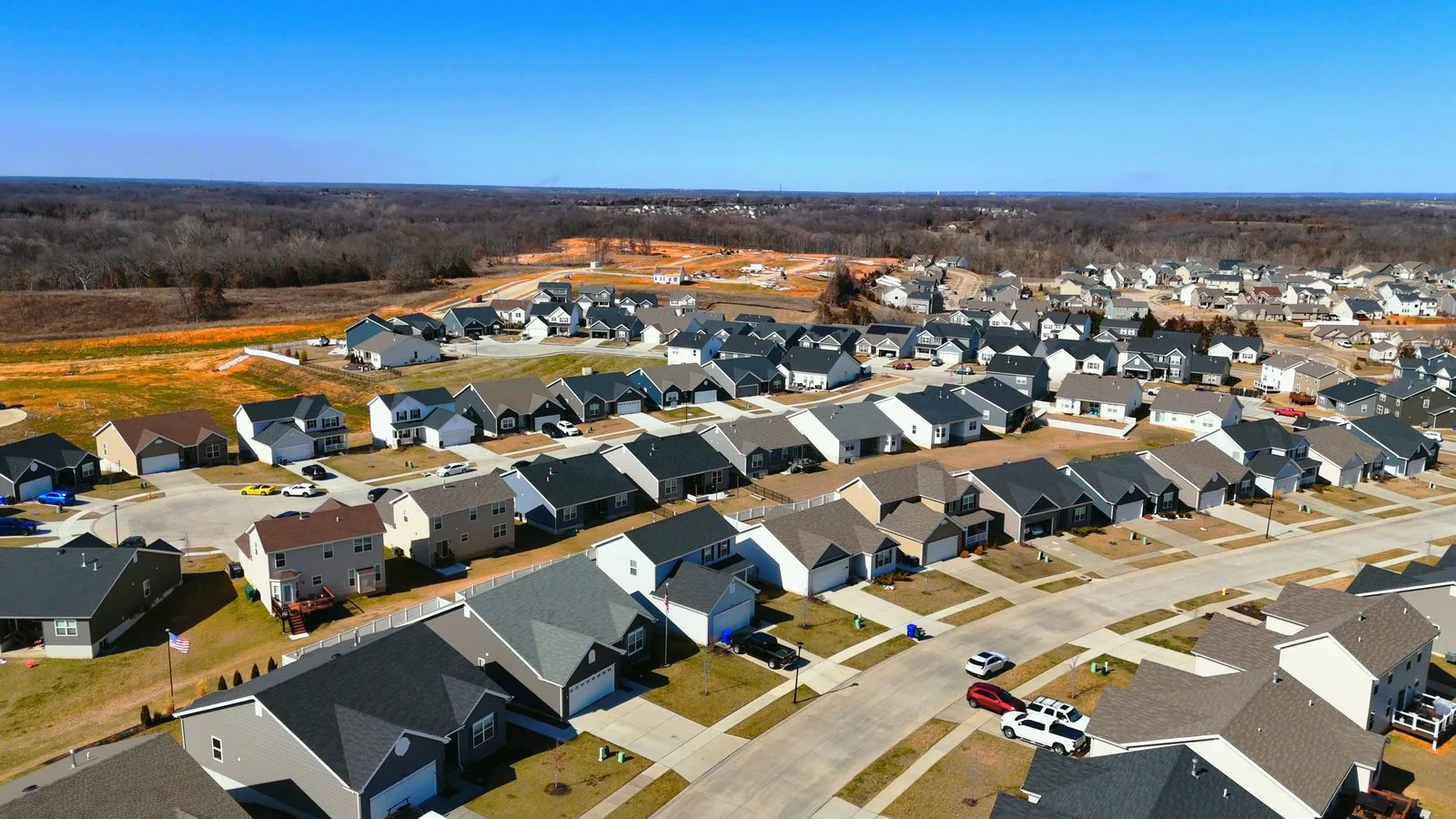 Aerial view of new homes and foundations under construction at Sutton Farms in Wentzville, with finished houses on the next street, February 2024