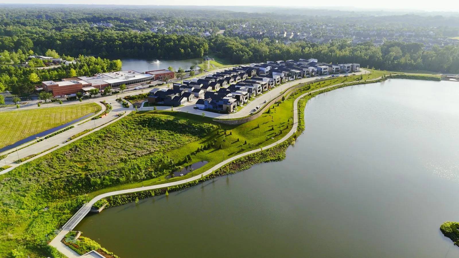 Aerial photograph of Wildhorse Village in June 2025 looking across the lake toward the terraced lawns, the walking path and the row of modern detached homes above them