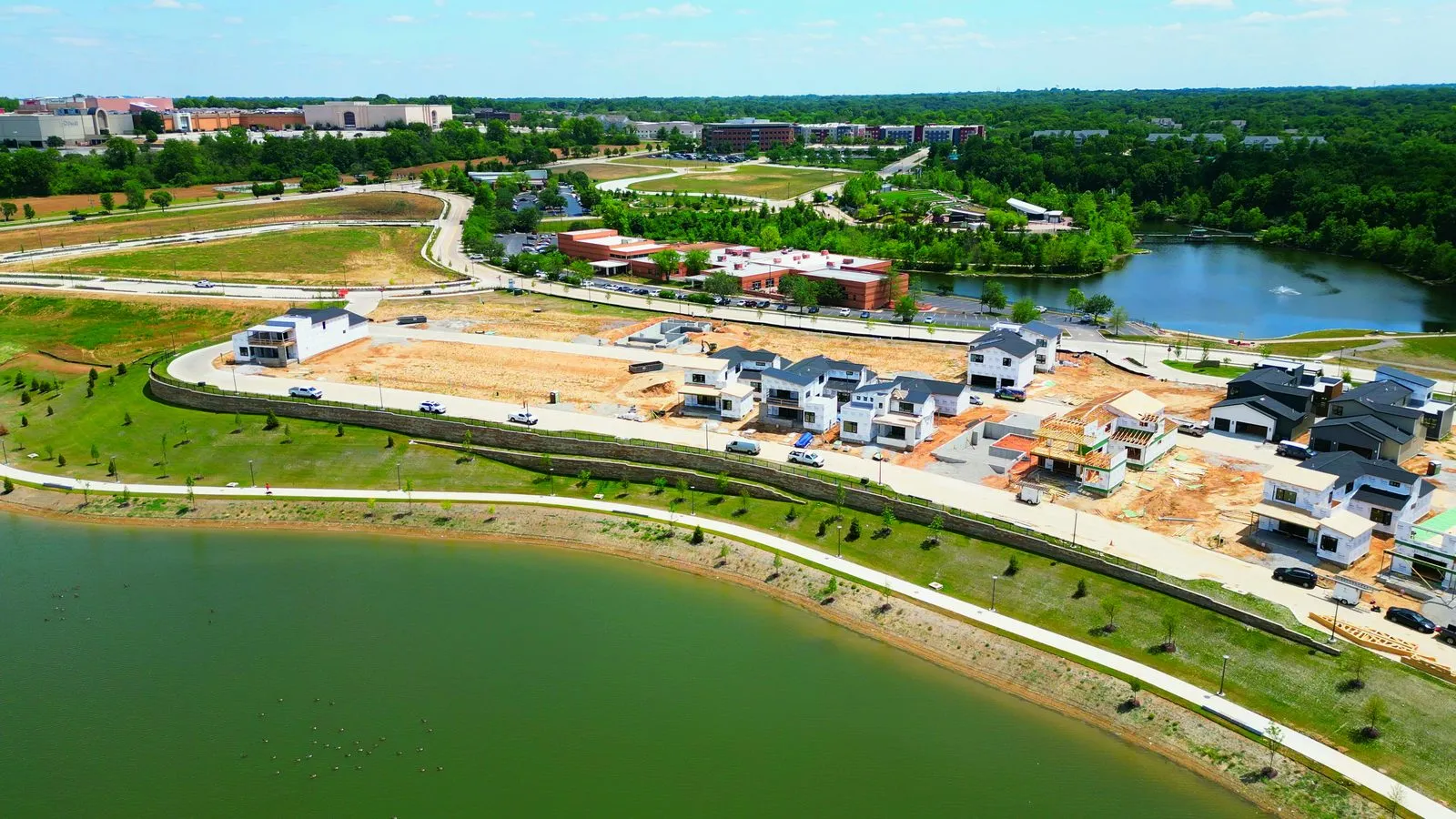 Aerial photograph of the Waterfront at Wildhorse in June 2023, with a handful of modern homes finished, several more in framing and bare graded dirt where the rest of the street will go, above the newly filled lake
