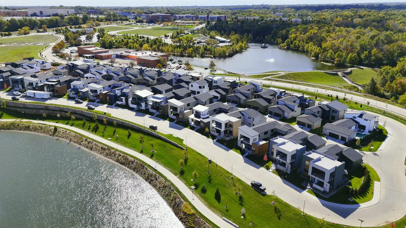 Aerial photograph of the modern detached homes at the Waterfront at Wildhorse Village in October 2024, flat and shed roofs in white, grey and wood, laid out in rows above the lake