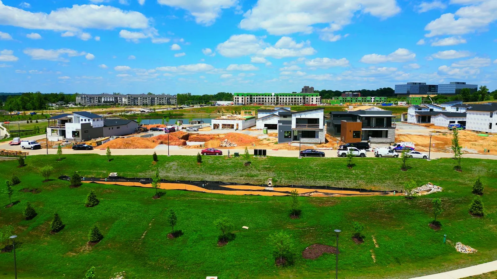 Aerial photograph of Wildhorse Village in June 2023 showing the new park lawn and terraced retaining walls beside the lake, with homes under construction on the ridge behind them
